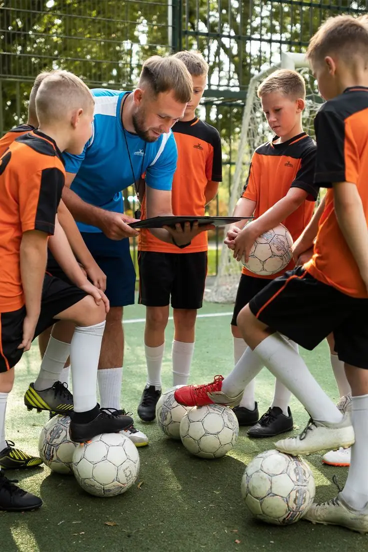 A coach with a clipboard among young footballers, each with a ball