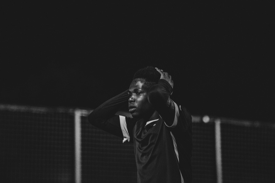 A footballer at a floodlit pitch at night, hands on his head